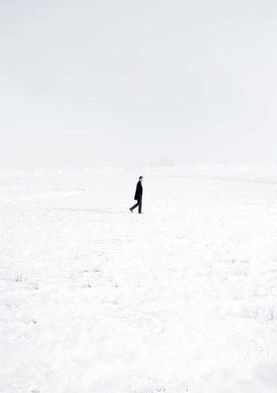 人白天黑色大衣走在冰雪覆盖领域
